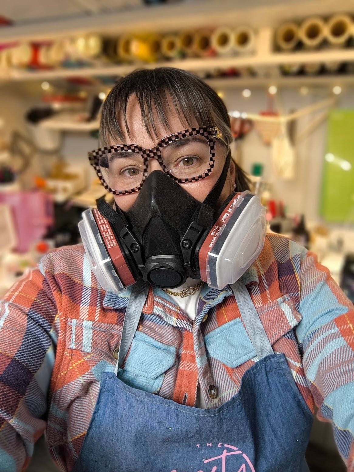 Kirsty in a respirator at her workbench, surrounded by reels of material