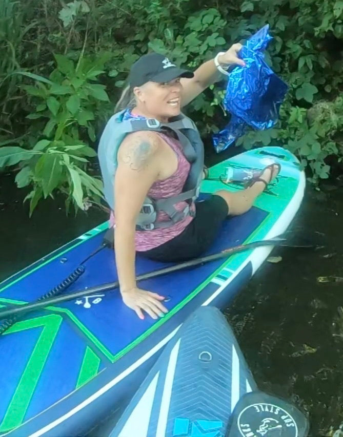 Kirsty sitting on her paddleboard on the river, holding up a crisp packet she has just fished out of the water
